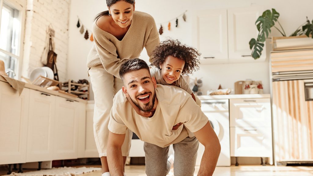 young family with young child smiling and playing together on floor of kitchen