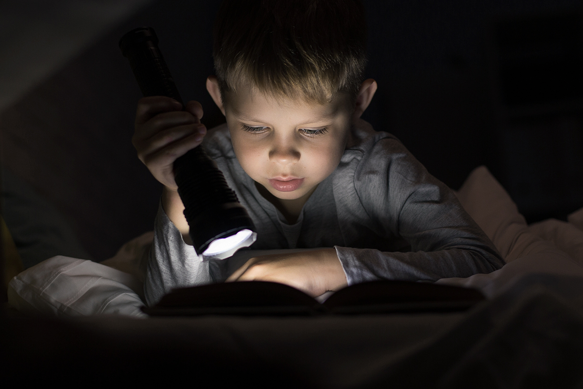 Young boy reading using in the dark with a flashlight
